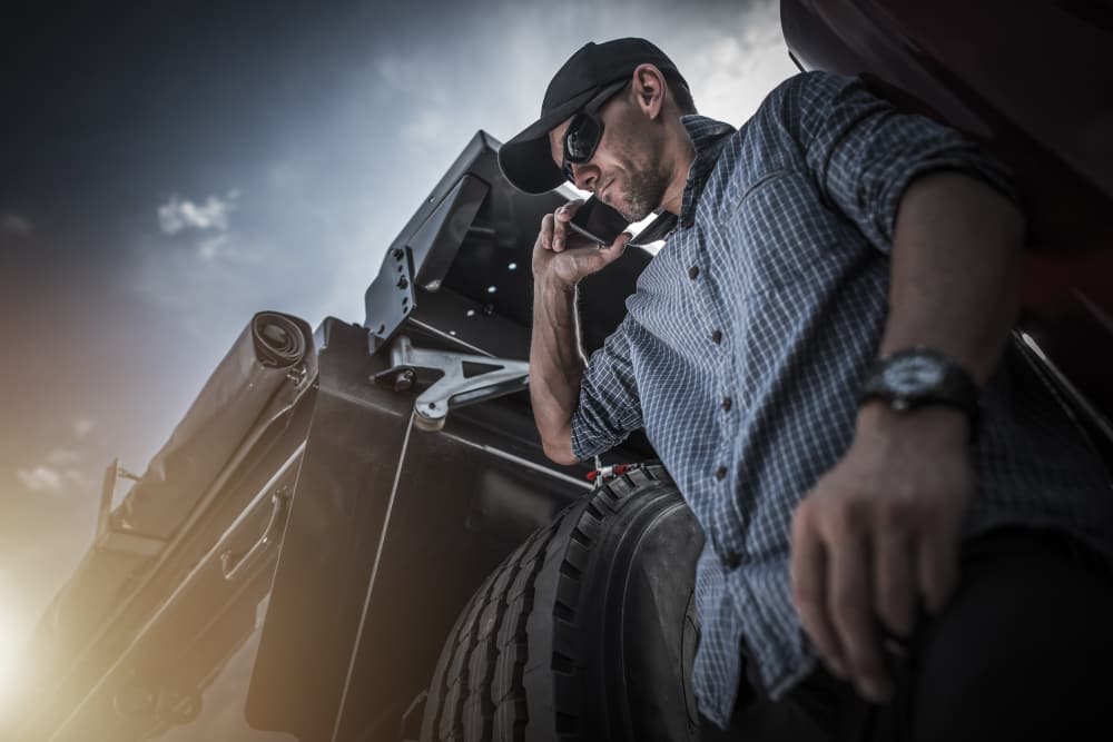 A dump truck driver on the phone beside the truck, coordinating a job